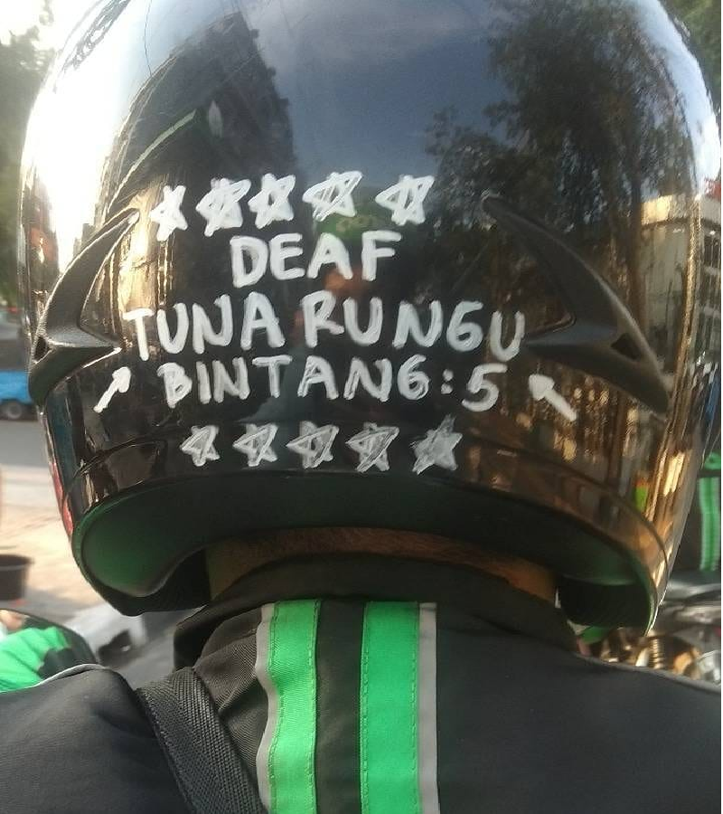 Tuna rungu driver ojek online ini berkomunikasi dengan penumpang lewat tulisan dibelakang helmnya